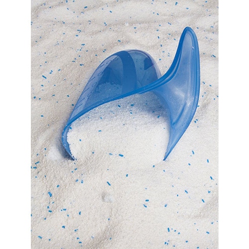 Blue plastic scoop half-buried in white laundry powder with blue speckles.