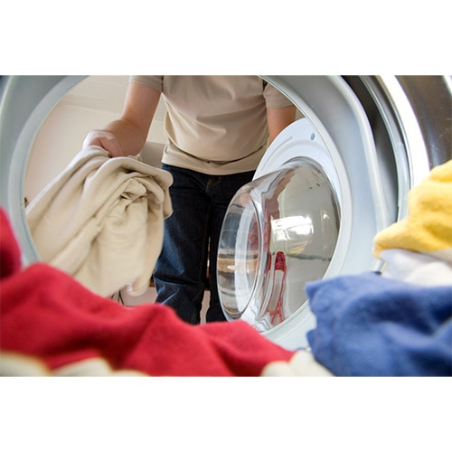 Person loading a front‑loader washing machine with light‑coloured laundry, view from inside the drum.