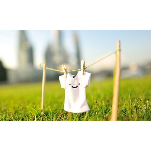 Tiny white T-shirt with smiley face pegged to a mini clothesline on grass, city skyline blurred behind