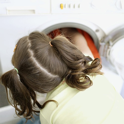 Child with pigtails leaning into open front-loading washing machine